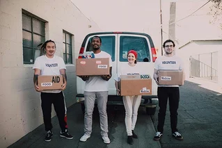 a group of volunteers smiling and waving at a beneficiary as they pass out donations 