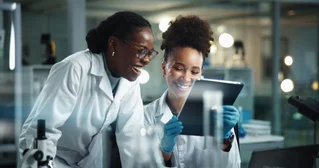 Two Black female scientists smiling and reviewing data in a lab