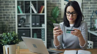 A woman in front of a computer with her phone and credit card in hand, donating online