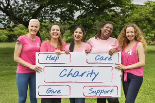 Women in pink shirts standing with sign that says charity