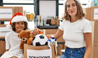 Woman standing with child wearing a santa hat sitting next to donations