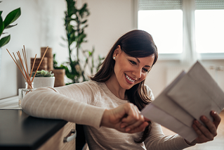 Woman smiling looking at three pieces of mail. 