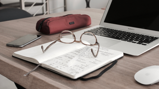 Notepad, computer and glasses on a desk. 