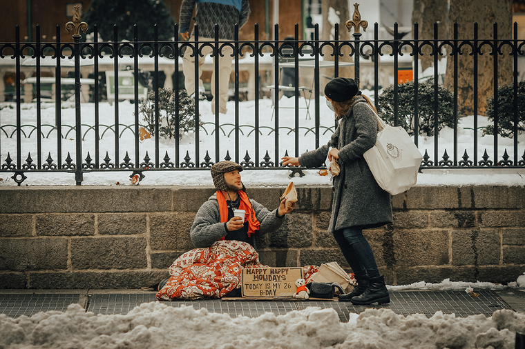 A pedestrian handing money to a person experiencing homelessness on the street