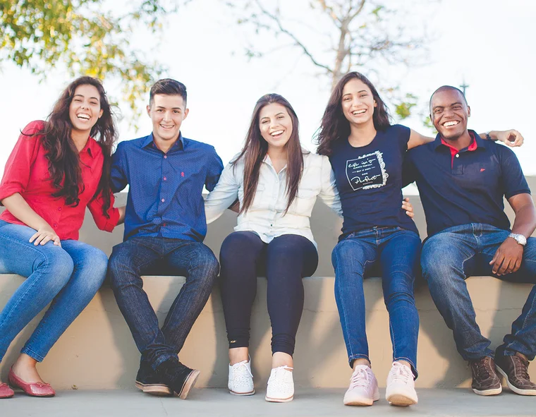 A group of happy individuals sit on a bench, smiling arm-in-arm
