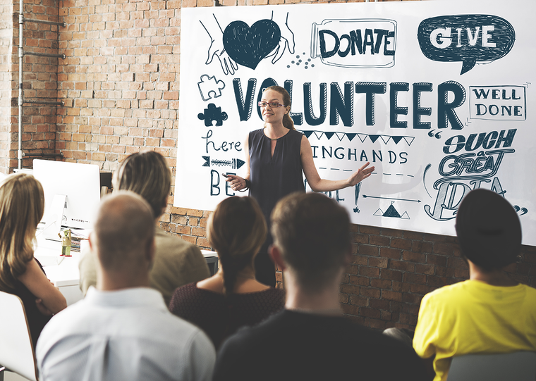 A woman stands in front of a crowd of volunteers, speaking about their activities for the day
