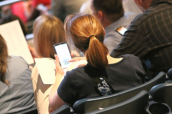 A woman sits in an auditorium for a charity auction, looking at her phone casting a mobile bid