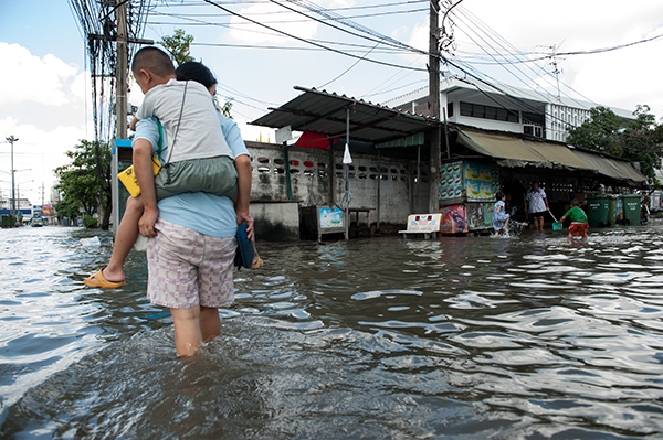 A parent carrying their child on their back through flood waters