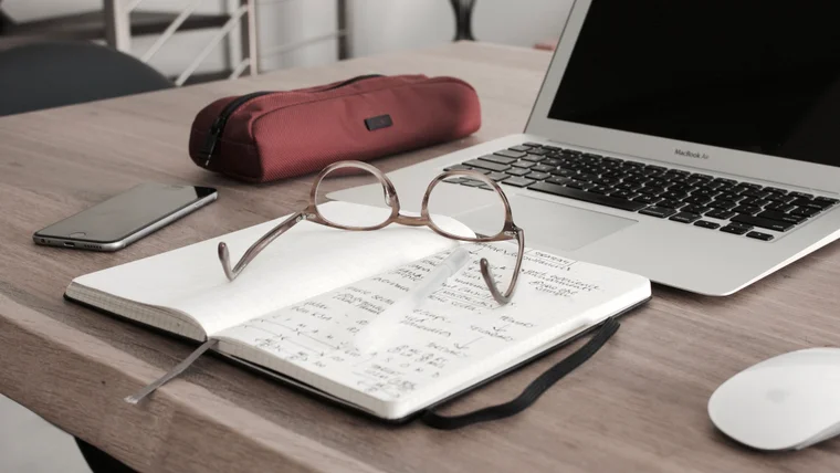 Image of a notebook and reading glasses sitting near an open laptop