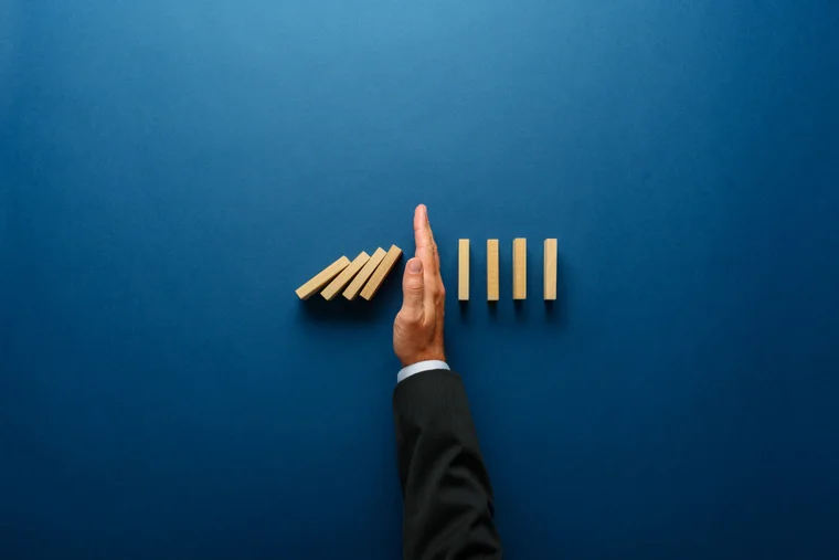 A hand blocking a stack of dominoes from falling