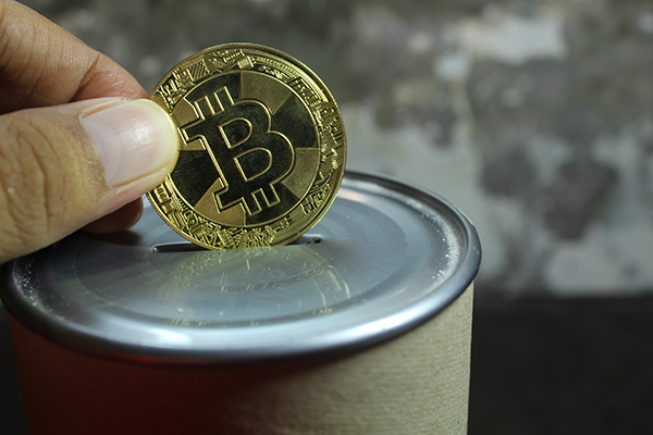 Someone donating a tangible bitcoin into a donation tin