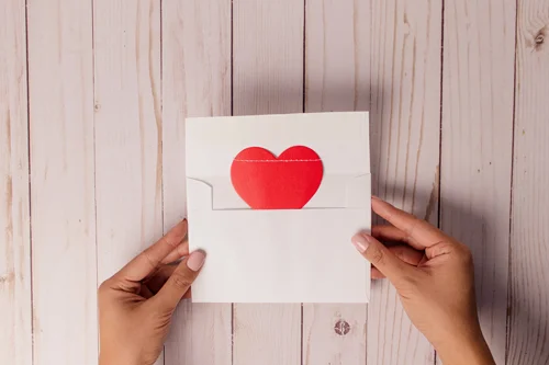 Someone holds an envelope that is open with a piece of paper and a heart