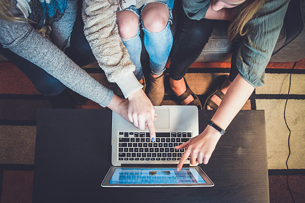 Overhead view of three friends pointing at the screen of their laptop