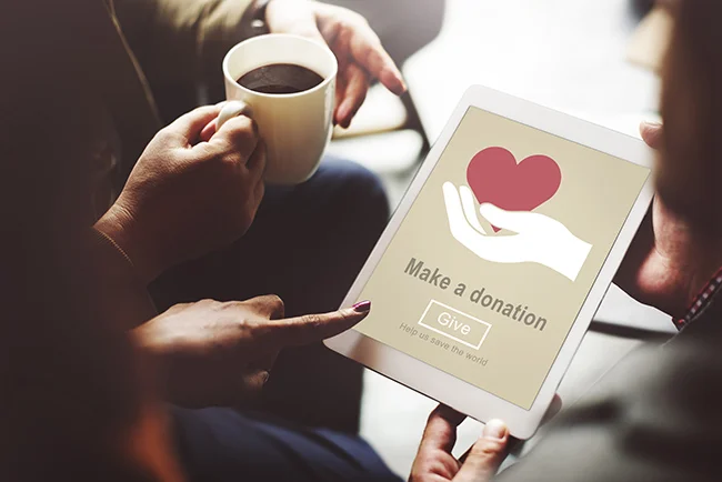An individual holds a tablet in their hand with a donation landing page and button on it's screen.