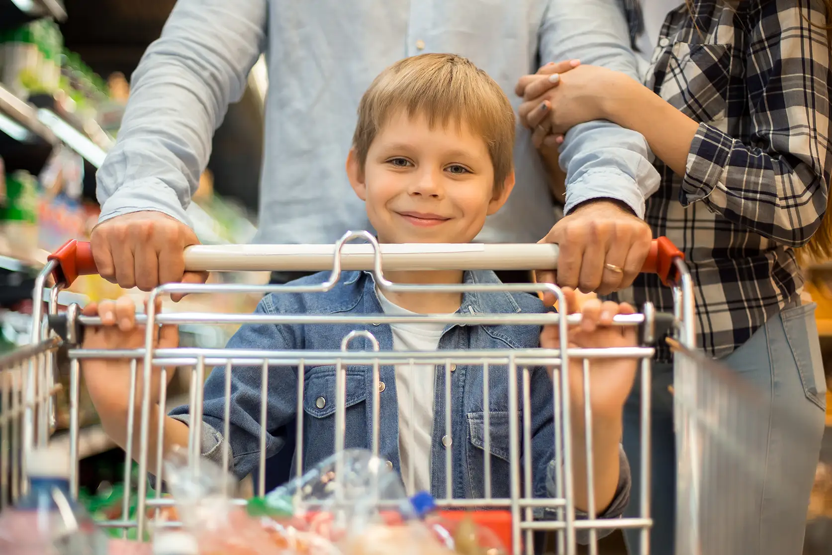 Smiling child pushing a grocery cart with parents, in a store.