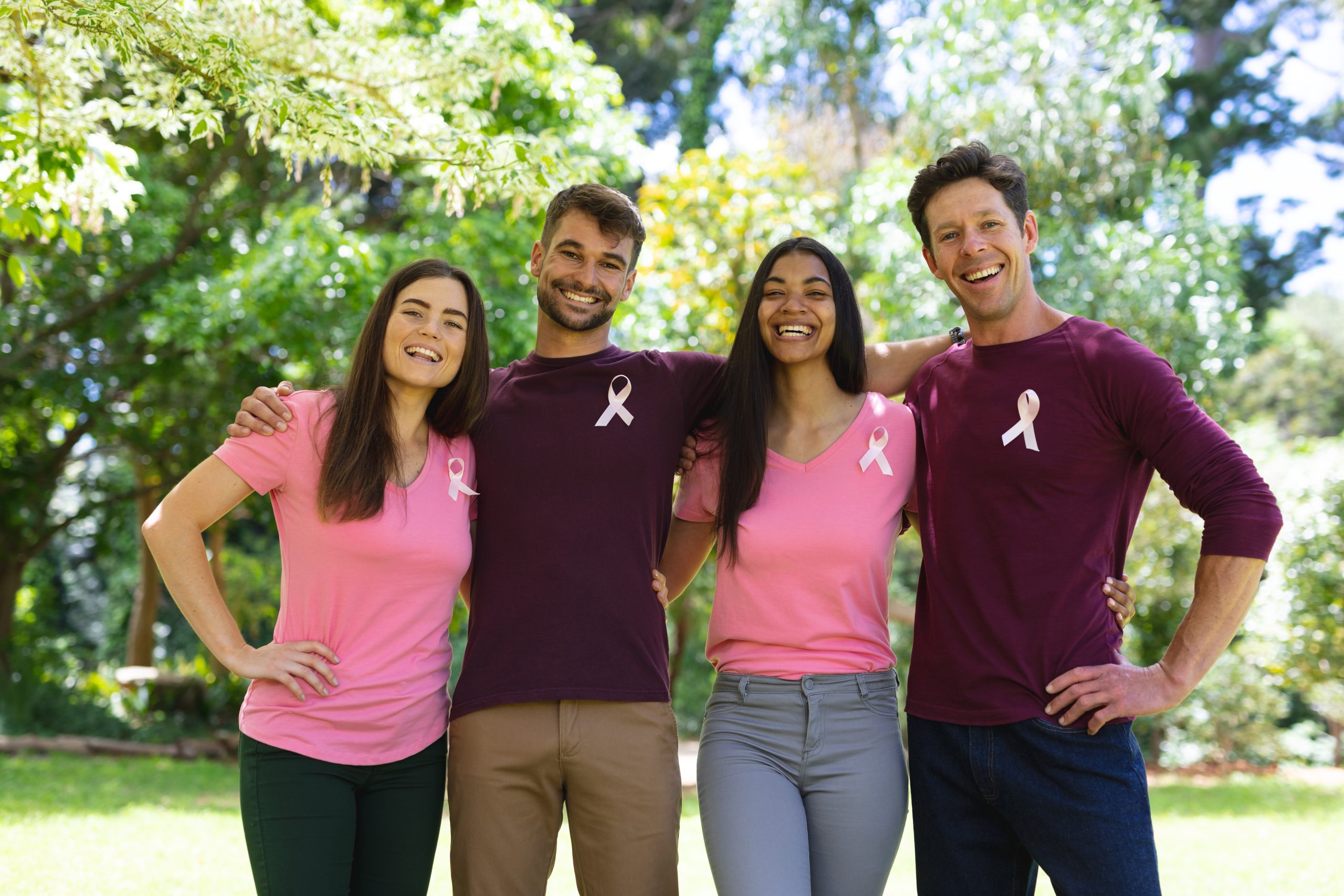 A group of four smiling adults, men and women, wearing pink ribbons